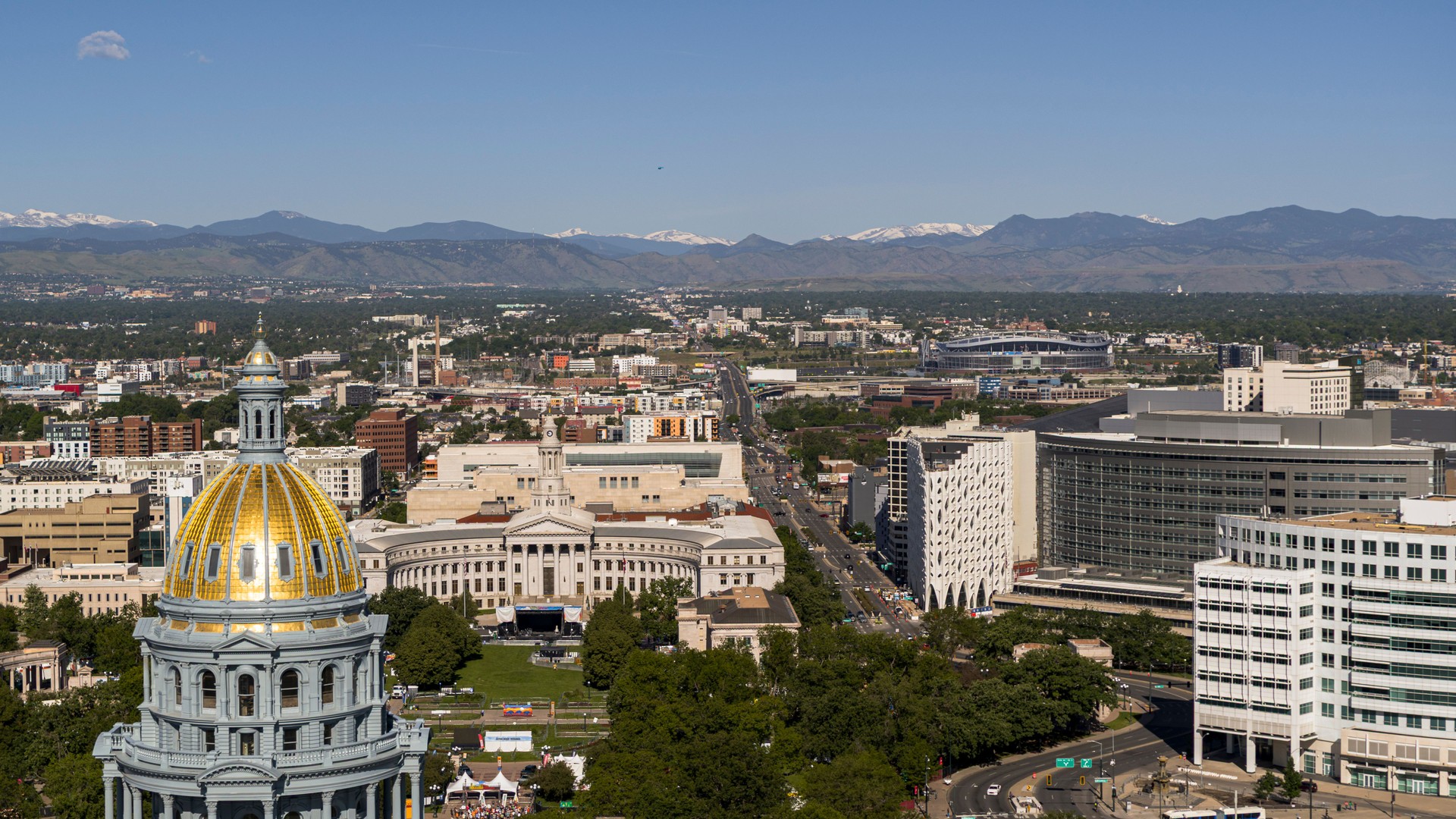 Rocky Mountain backdrop frames city center of Denver, Colorado. City and County Building and Civic Center Parkvisible with sports stadium in distance.